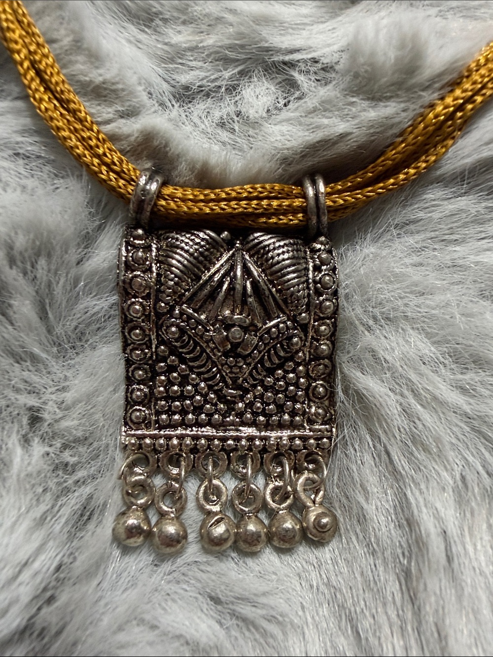 Silver tribal amulet pendant attached to a multi-strand mustard-yellow cord